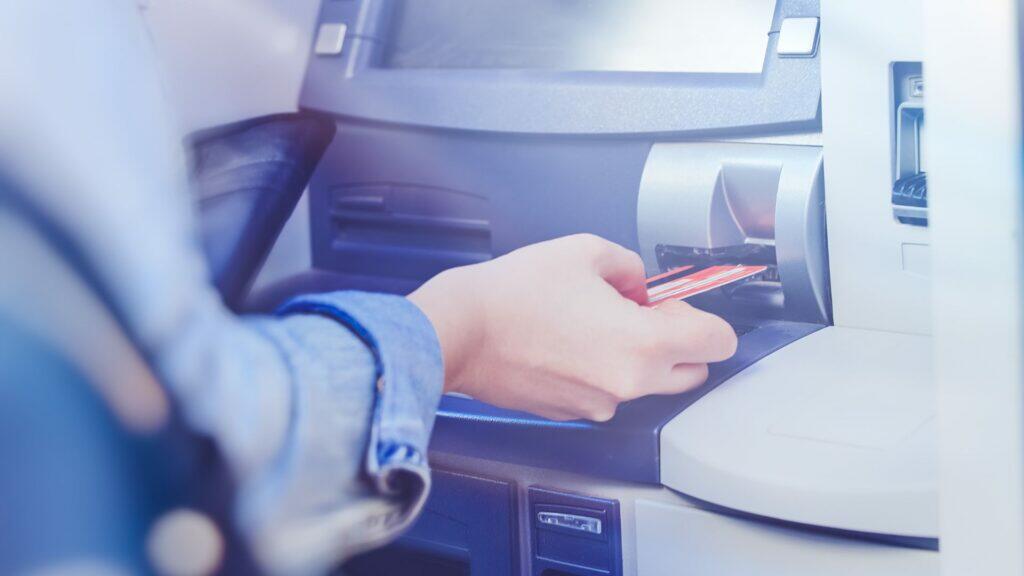 Eine Person steckt eine Kreditkarte in einen Geldautomaten. Symbolbild Bankautomat.